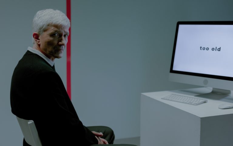 Starszy mężczyzna przed komputerem, w tle czerwona linia